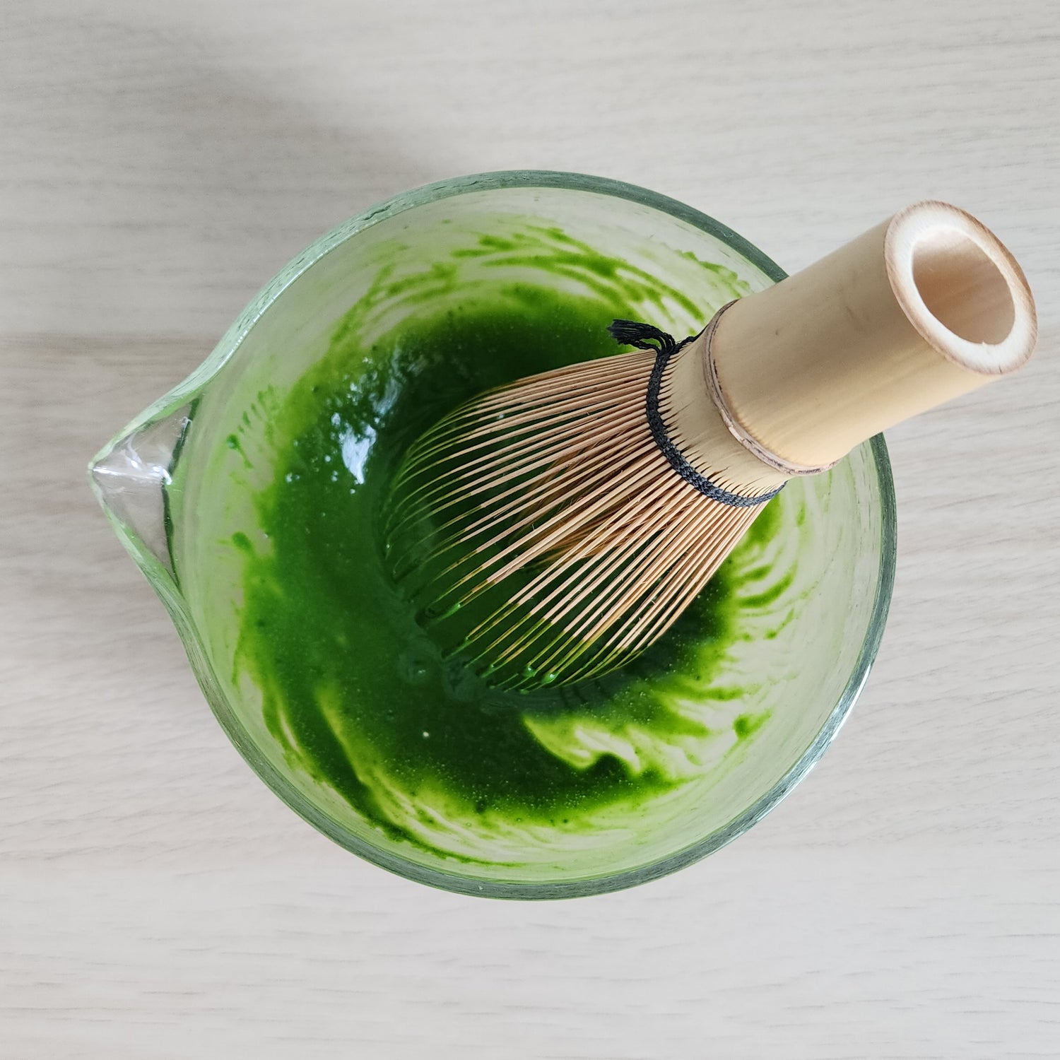 Matcha bamboo whisk (chasen) stirring fresh green matcha in a glass bowl—ideal for achieving the perfect froth