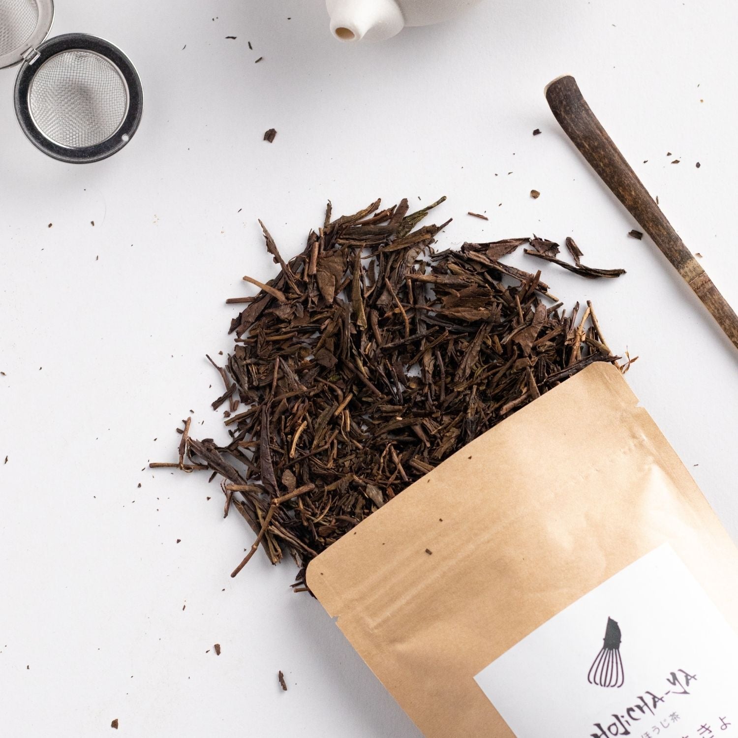Premium roasted loose leaf Hojicha tea  with a deep, smoky aroma, elegantly spilled from a kraft pouch