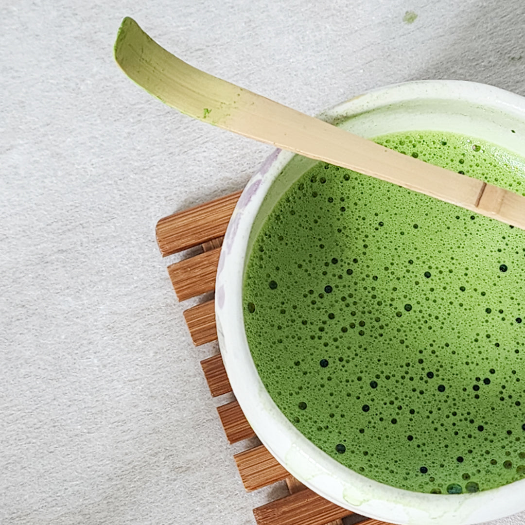Matcha bamboo scoop (chashaku) resting on a chawan filled with frothy green tea, showcasing traditional Japanese tea-making